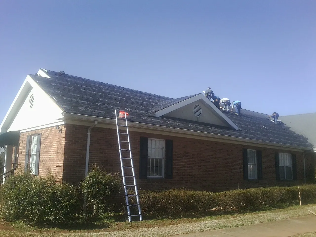 Crew tearing shingles off a brick ranch roof with a ladder set — Metal Roof Repair work by our crew in Folkston