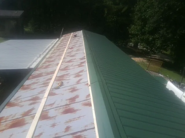 Old rusted panels beside newly installed green metal roofing — Wind Damage Roof Repair by Roofing Brothers in Folkston
