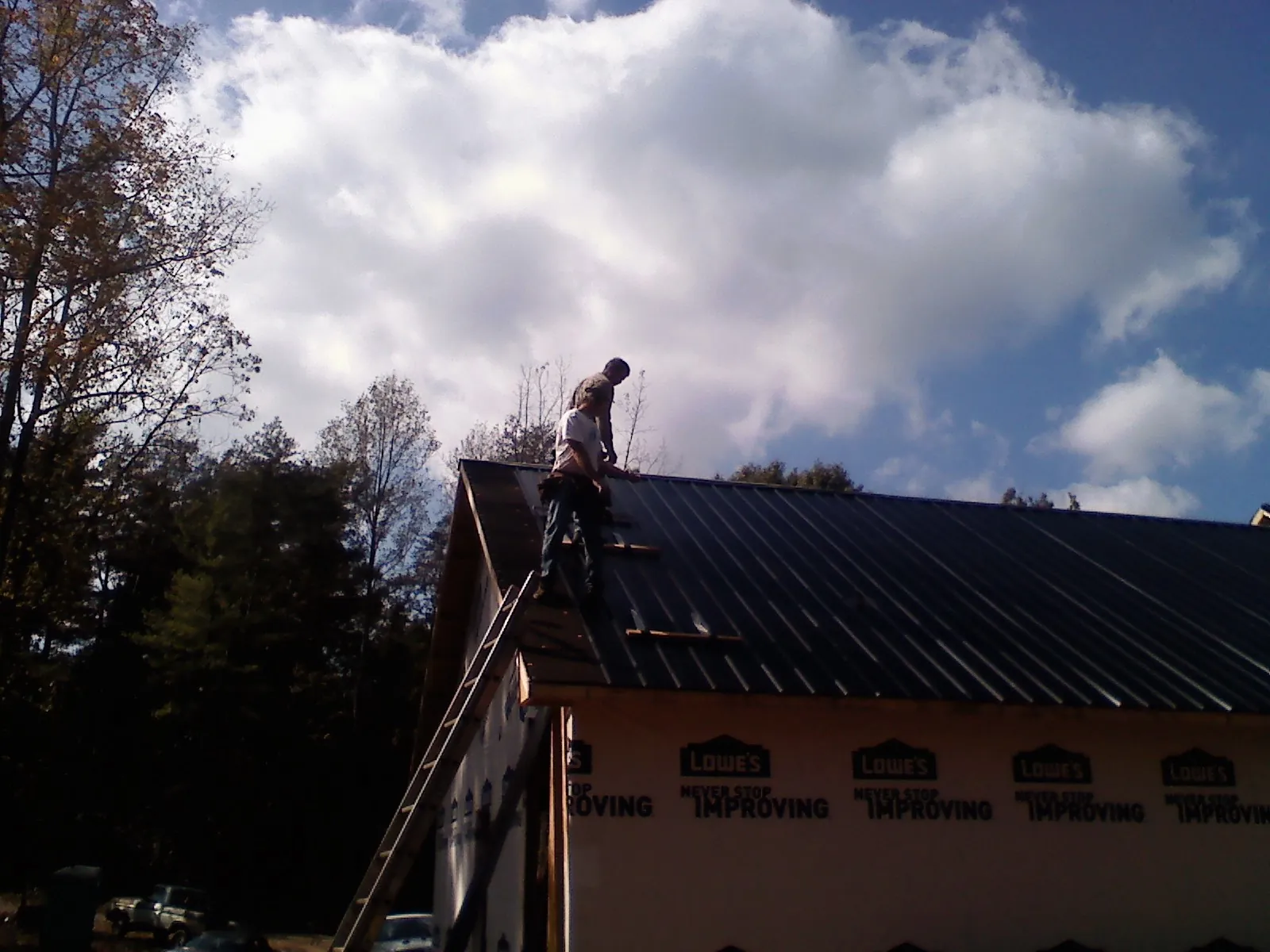 Roofer fastening dark metal panels high against a cloudy sky, from a Roof Inspection job in Folkston