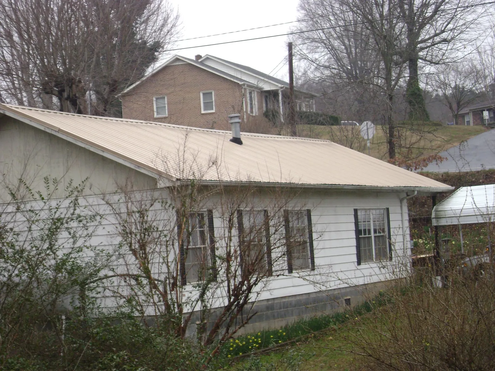 Tan metal roof on a white sided house set into a hillside — Commercial Roofing by Roofing Brothers in Folkston